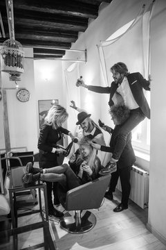 Gruppo di parrucchieri si divertono e lavorano su una bellissima modella bionda 