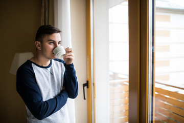 handsome man drinking coffee next to a window inside the house