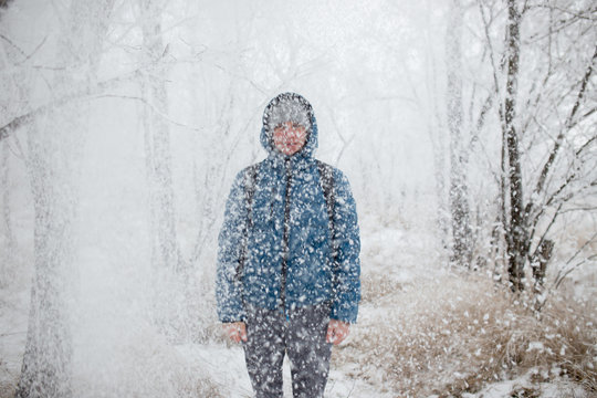 Young handsome man standing in snowfall on background of snowy forest.