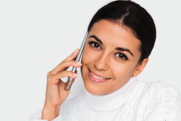 Beautiful portrait of attractive young happy woman with mobile phone with pretty toothy smile, on the white background. Brunette woman using smart phone looking in front.