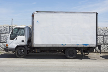 Parked used white delivery van parked in front of stone wall Horizontal..