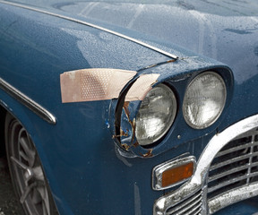 Ouch...Large bandage on classic car's fender and headlight. Horizontal