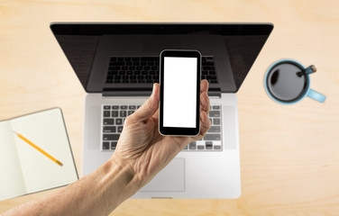 Hand holding smartphone with blank screen over desk