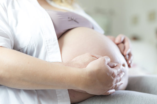 Schwangere Frau und Partner halten Hände schützend um Babybauch