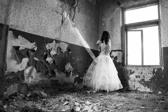Sad mood in an old, abandoned house with girl half dressed at the natural light from the window.  Artistic black and white photography