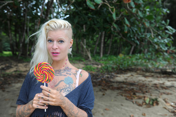Tattooed girl with big lollipop on the beach 