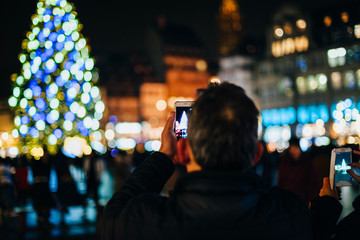 Rear view of male taking on smartphone a picture of the Christmas Tree in central square of Strasbourg, France during the iconic Christmas Market