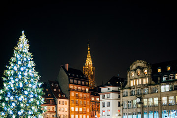 Christmas market atmosphere with majestic Christmas Tree and the illuminated Notre-Dame Cathedral - seen from Place Kleber in Strasbourg, France Alsace