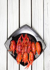 Steamed crayfish on the black rectangular plate. Fresh boiled crawfish with spices. Rustic style. Wooden background.