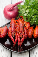 Fresh steamed crayfish on the black rectangular plate. Boiled crawfish with parsley and spices. Rustic style. Wooden background.