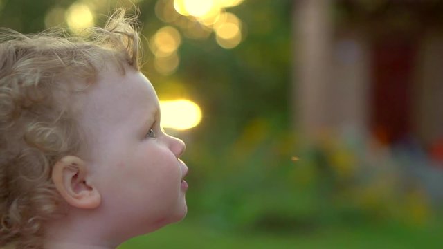 Adorable baby girl playing in summer park. Beautiful 1 year old child close up portrait over nature green background, emotions. Slow motion 240 fps, Full HD 1080p. High speed camera