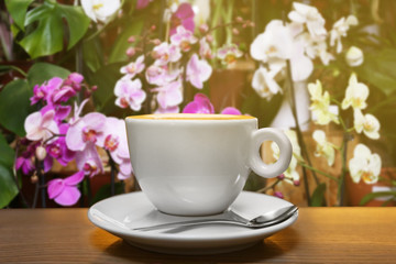 Fototapeta na wymiar Cup of aromatic coffee on table against blurred floral background. Flower bar concept