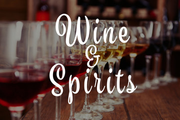 Text WINE AND SPIRITS on background. Glasses of different wine in row on table