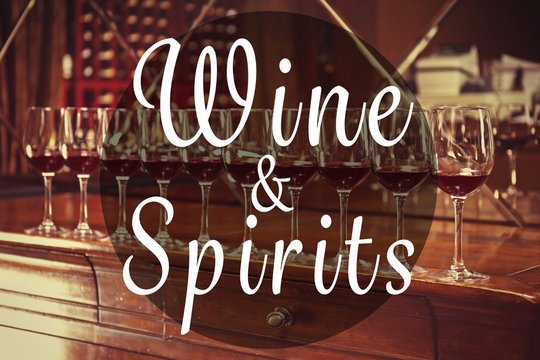 Text WINE AND SPIRITS on background. Row of glasses with red wine on bar counter