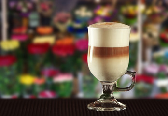 Glass cup of aromatic coffee on table against blurred floral background. Flower bar concept