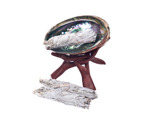 Sage smudge stick and bright polished rainbow abalone shell with wooden cobra stand isolated on...