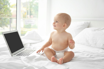 Cute baby boy with laptop on bed