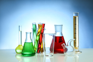 Chemical flasks and test-tubes on color background