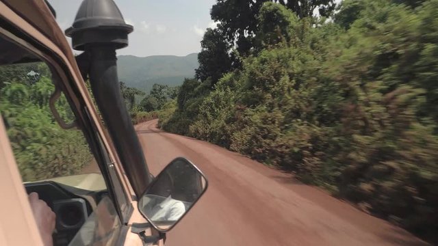 CLOSE UP: Safari jeep game driving tourists in lush African jungle on dusty road