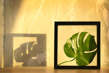 Black frame with green leaf on wooden table
