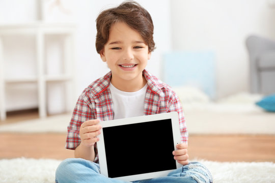 Cute little boy sitting on the carpet with tablet on blurred background