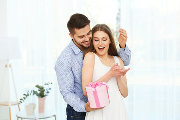 Handsome young man giving present to beautiful woman at home