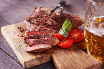 Grilled steak with tomatoes on cutting board and mug of beer, closeup