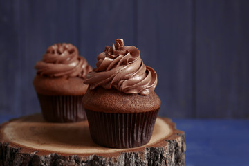 Tasty chocolate cupcake on wooden stand against dark background
