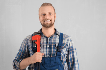 Fototapeta premium Portrait of handsome plumber with pipe wrench on light background