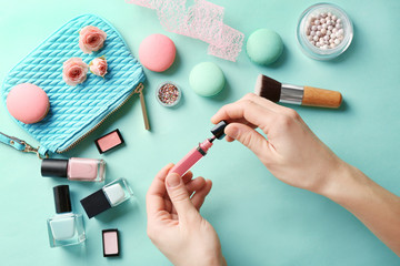 Woman holding lipgloss over makeup products and macaroons