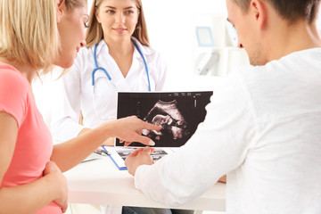 Gynecology consultation. Doctor showing ultrasound scan  of baby to couple