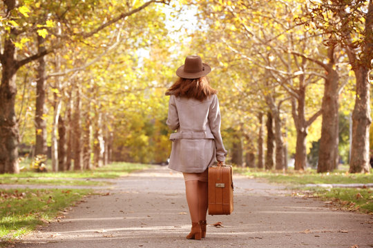 Beautiful young woman with suitcase in a autumn park