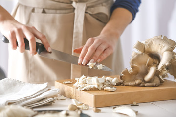 Obraz na płótnie Canvas Woman cutting mushrooms on wooden board at kitchen, closeup
