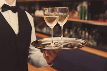 Young handsome waiter holding tray with wine glasses in the restaurant