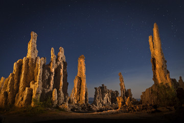 Tufa formation at Mono Lake at night with stars in the sky. Shallow depth of field with focus on lit prominent rock formations