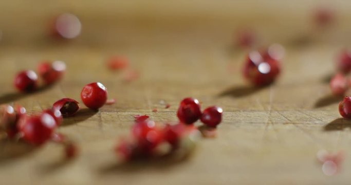 grains of pepper pink pepper colorful in extreme slow-motion fall on a wooden surface and mingle with each other 