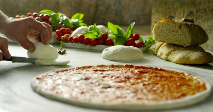 Super slow motion of a middle aged chef cutting mozzarella of bufala cheese for pizza on a restaurant kitchen table in 4k (close up)