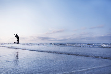 Woman jumping for joy on beach at sunrise