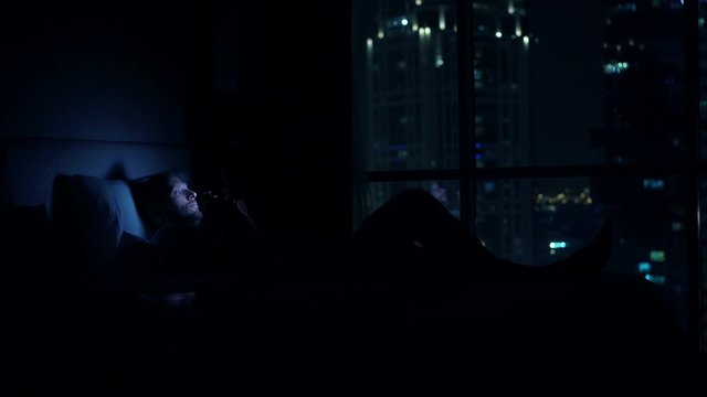 Man waking up and using smartphone on bed at home at night
