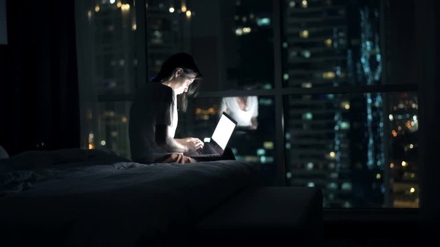 Young woman finish working on laptop and falling asleep in bedroom at night
