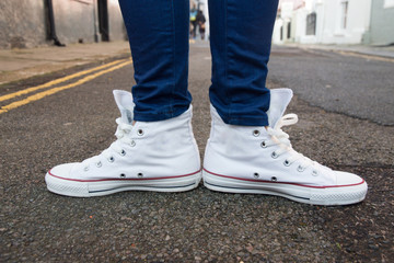Close-up of female feet in fashionable sneakers are standing on the sidewalk.