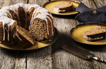 Banana cake with apples and walnuts drizzled frosting and sliced pieces on plates with effect craquelure on the shabby wooden background. Selective focus 