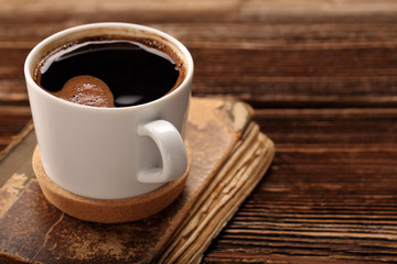 Cup of coffee and old book on wooden background