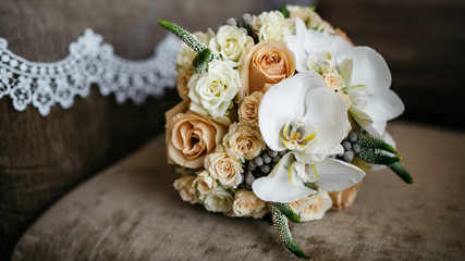 Beautiful wedding bouquet of beige roses and white irises lying on the sofa. White lace on a background. Space for text