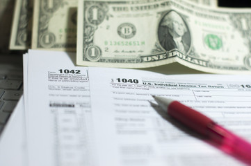 Tax Season: 1040 U.S. Individual Income Tax Return Form horizontal top view with an office laptop and blue calculator as background together with a red white pen preparation on taxation as foreground