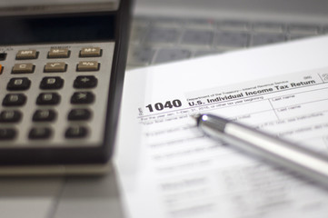 Tax Season: 1040 U.S. Individual Income Tax Return Form horizontal top view with an office laptop and blue calculator as background together with a red white pen preparation on taxation as foreground