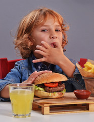 niño contento comiendo hamburguesa y patatas fritas.