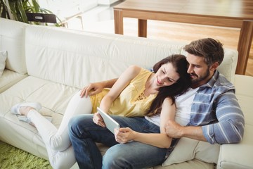 Obraz premium Happy couple using digital tablet while relaxing on sofa