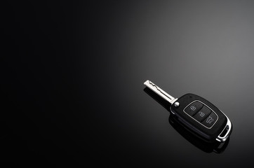 Modern car keys isolated on black reflective background with copy space for text or design elements. Folding key with remote alarm and trunk opening