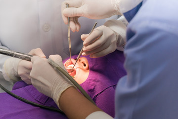 dentist and assistant wearing glove cleaning teeth while patient open mouth